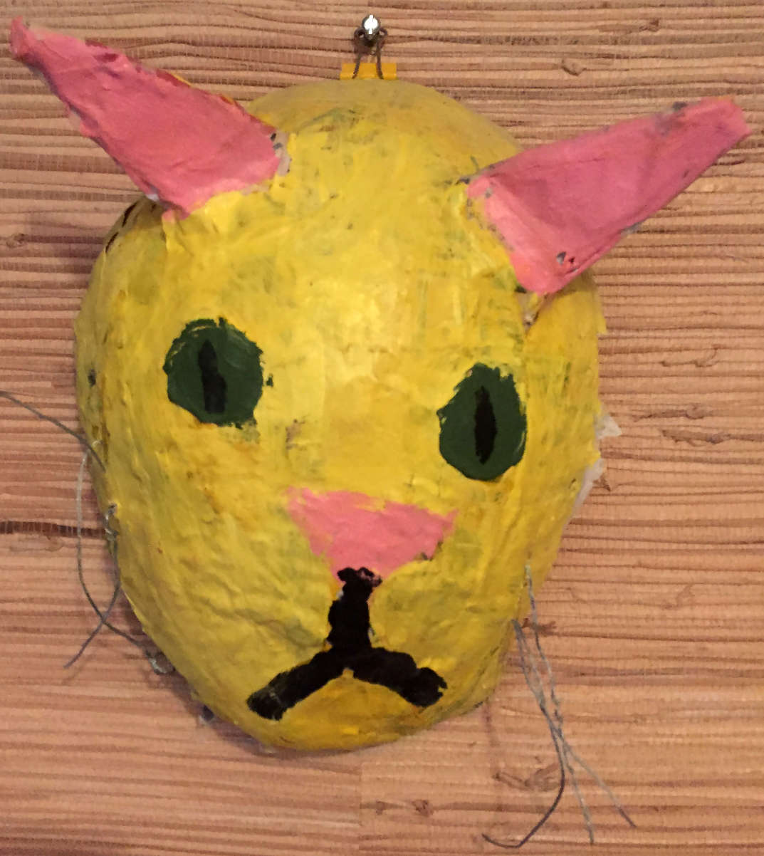 A yellow mask that looks like a cat and has pink ears.
